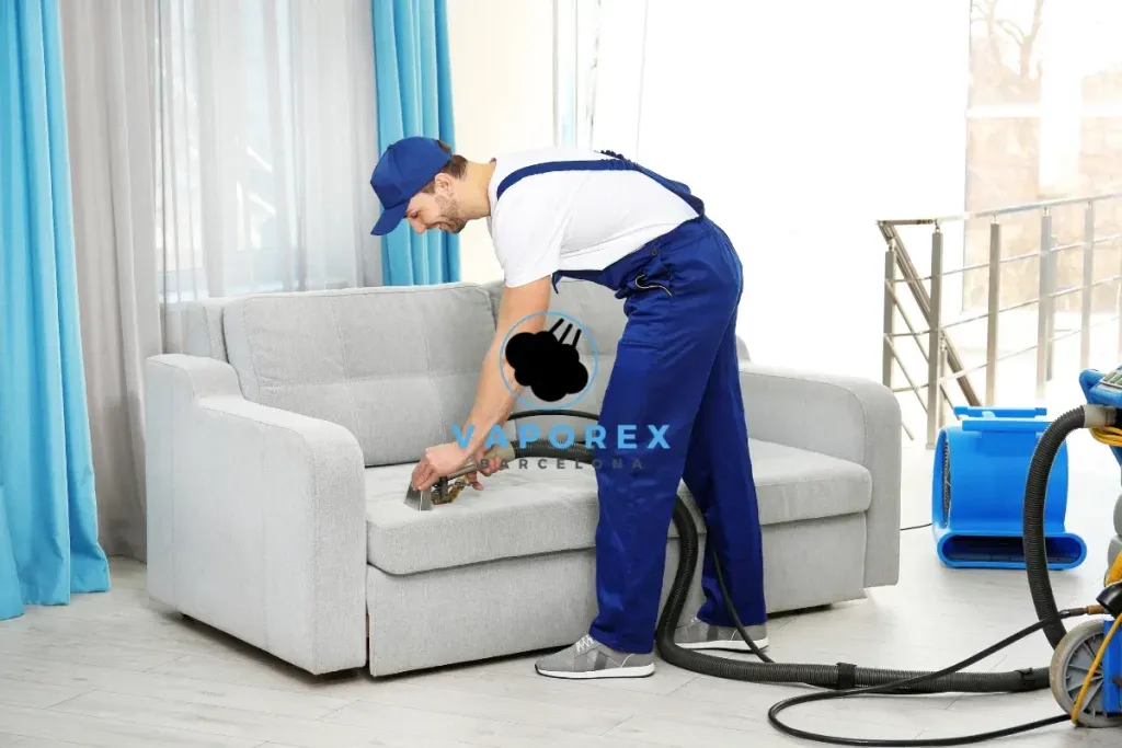Técnico de Vaporex limpiando con inyección-extracción un sofá gris de zona lounge junto a un ventanal
